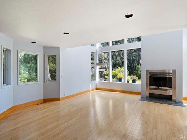 unfurnished living room featuring baseboards, a fireplace with flush hearth, and hardwood / wood-style flooring