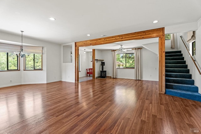unfurnished living room featuring a wood stove, wood finished floors, stairway, baseboards, and recessed lighting