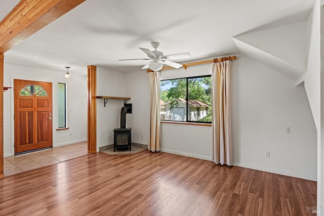unfurnished living room featuring baseboards, a wood stove, ceiling fan, and wood finished floors