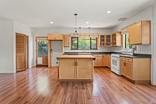 kitchen featuring visible vents, light brown cabinetry, a center island, a sink, and white range with gas cooktop
