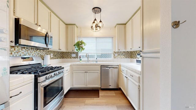 kitchen with a sink, light wood-style flooring, stainless steel appliances, tile countertops, and tasteful backsplash