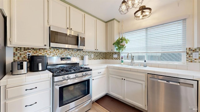kitchen featuring decorative backsplash, appliances with stainless steel finishes, a sink, white cabinets, and tile counters