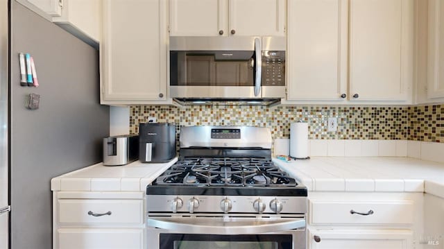 kitchen featuring backsplash, stainless steel appliances, tile counters, and white cabinetry