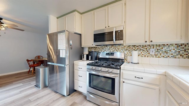kitchen with decorative backsplash, stainless steel appliances, tile counters, and a ceiling fan