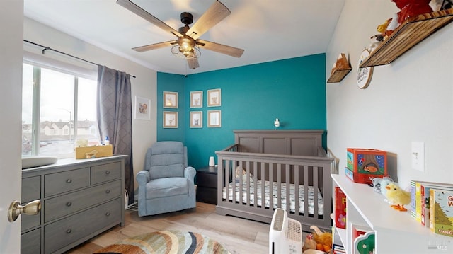 bedroom featuring a nursery area, ceiling fan, and wood finished floors