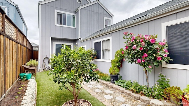 back of property with fence, a shingled roof, and a yard