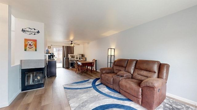living room with a multi sided fireplace, baseboards, a ceiling fan, and wood finished floors