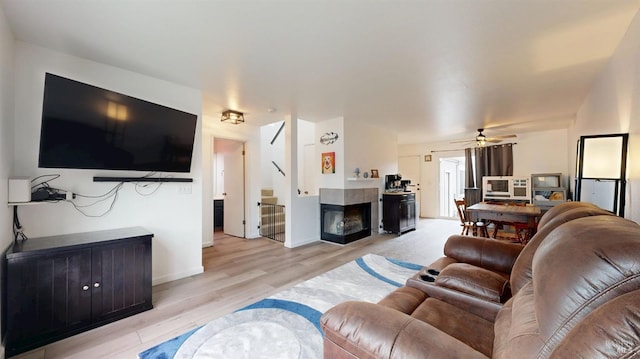 living room with a multi sided fireplace, baseboards, a ceiling fan, and light wood-type flooring