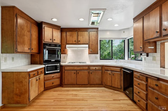 kitchen with under cabinet range hood, light wood-type flooring, black appliances, and brown cabinets