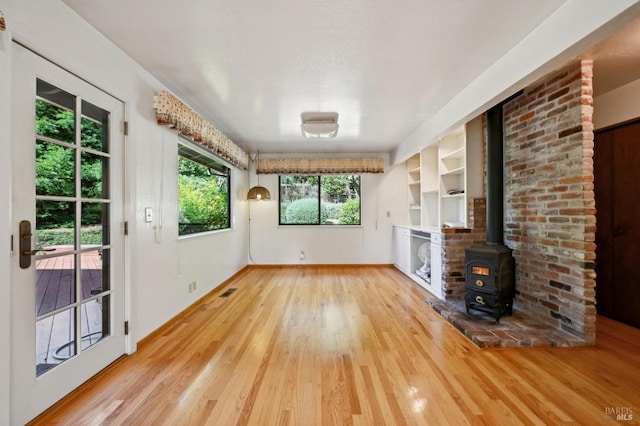 unfurnished living room with baseboards, a wood stove, visible vents, and wood finished floors