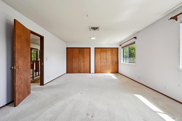 unfurnished bedroom featuring carpet flooring, multiple windows, two closets, and visible vents