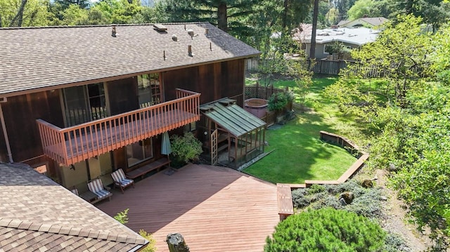 back of house featuring a wooden deck, a shingled roof, fence, and a lawn