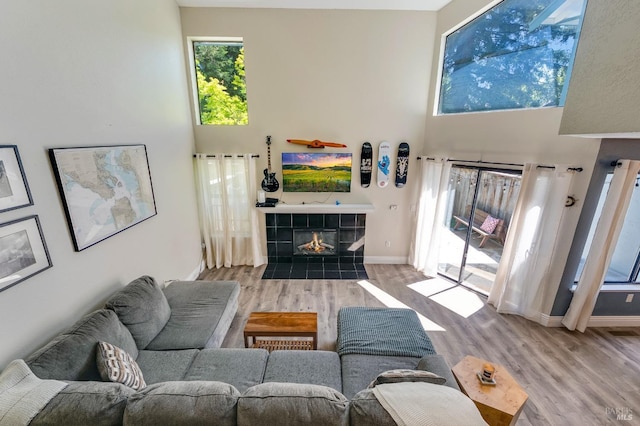 living room featuring baseboards, a towering ceiling, wood finished floors, and a tiled fireplace