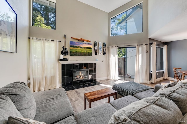 living area featuring a tiled fireplace, a wealth of natural light, wood finished floors, and a towering ceiling