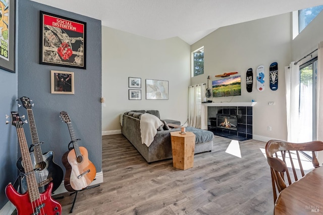 living area featuring baseboards, wood finished floors, a tiled fireplace, and high vaulted ceiling