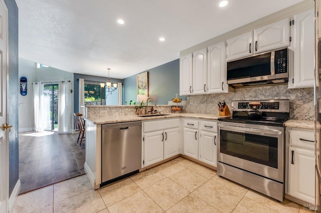 kitchen featuring backsplash, a sink, a peninsula, an inviting chandelier, and stainless steel appliances