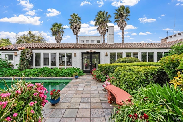 back of property featuring french doors, a chimney, a tile roof, and stucco siding