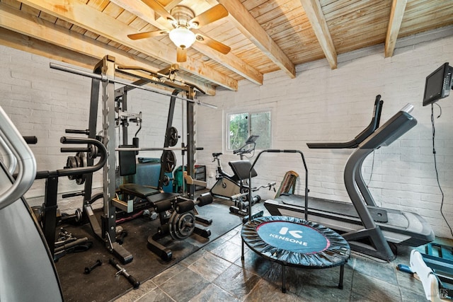 exercise room with wood ceiling, ceiling fan, stone finish flooring, and brick wall
