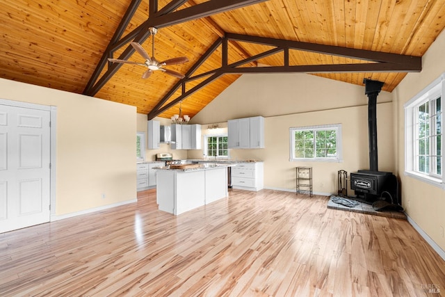unfurnished living room featuring wood ceiling, a wood stove, light wood finished floors, and beam ceiling