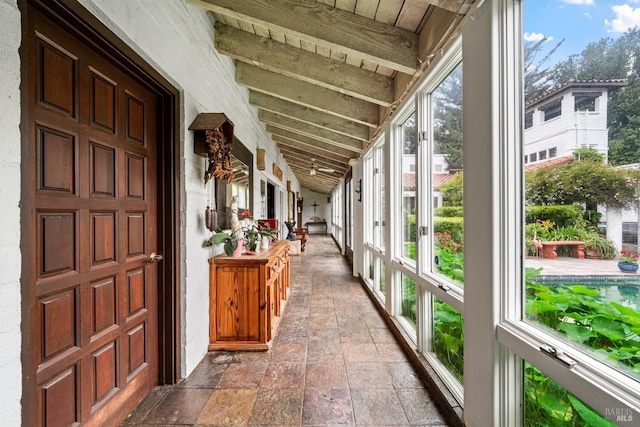 unfurnished sunroom featuring stone tile floors and vaulted ceiling with beams