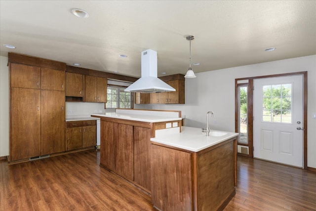 kitchen with brown cabinets, dark wood-style flooring, a sink, a center island, and island range hood