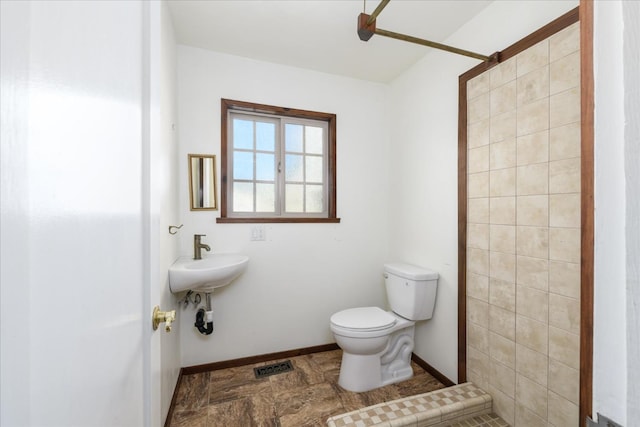 bathroom with a tile shower, a sink, toilet, baseboards, and visible vents