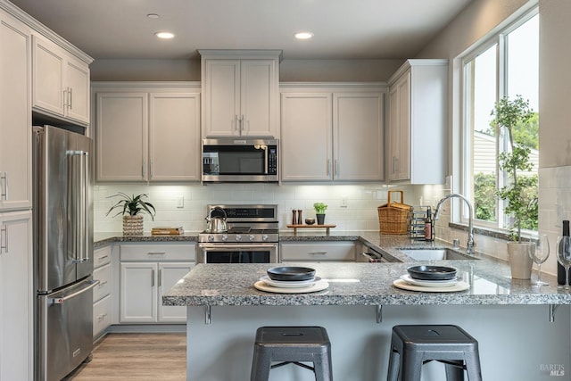 kitchen with appliances with stainless steel finishes, tasteful backsplash, a sink, light stone counters, and a peninsula