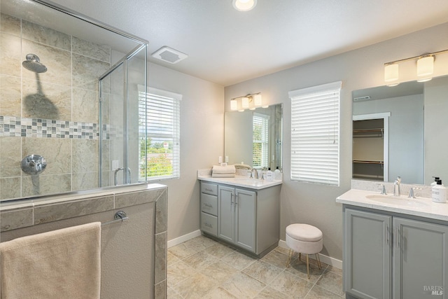 bathroom featuring visible vents, a stall shower, two vanities, a sink, and baseboards