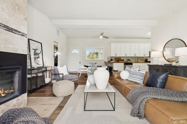 living room featuring a ceiling fan, beamed ceiling, wood finished floors, and a fireplace
