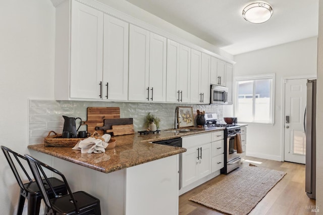 kitchen with white cabinetry, appliances with stainless steel finishes, a sink, and tasteful backsplash