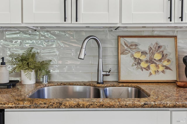 interior details with backsplash, white cabinetry, a sink, and dark stone counters