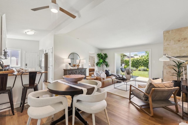 dining room featuring vaulted ceiling with beams, a fireplace, light wood finished floors, and ceiling fan