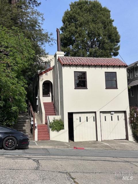 mediterranean / spanish home with driveway, a tile roof, an attached garage, stairs, and stucco siding