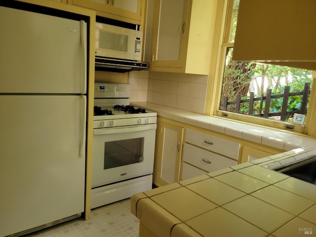 kitchen with tile countertops, backsplash, a healthy amount of sunlight, and white appliances