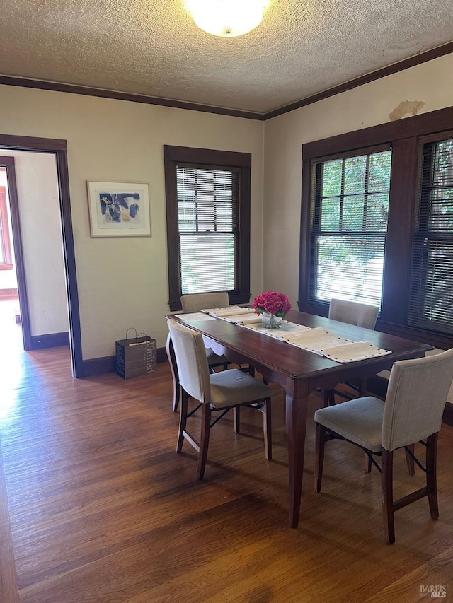 dining space featuring baseboards, a textured ceiling, ornamental molding, and wood finished floors