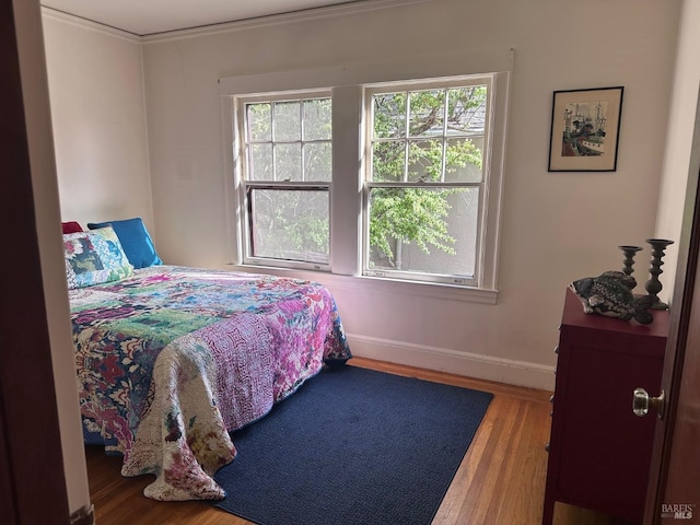 bedroom with baseboards, ornamental molding, and wood finished floors