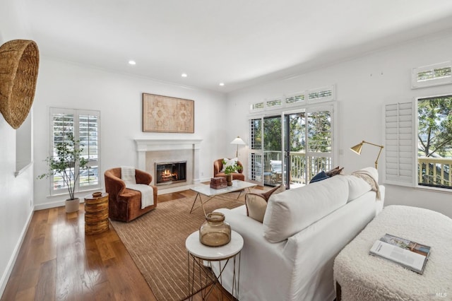 living room with ornamental molding, wood finished floors, baseboards, recessed lighting, and a fireplace with flush hearth