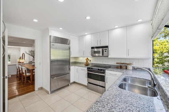 kitchen with a sink, appliances with stainless steel finishes, white cabinets, and light stone counters