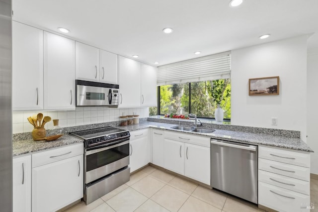 kitchen with white cabinets, light stone counters, a sink, backsplash, and stainless steel appliances