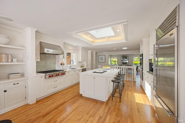 kitchen featuring exhaust hood, white cabinets, light wood-style floors, stainless steel appliances, and a kitchen island