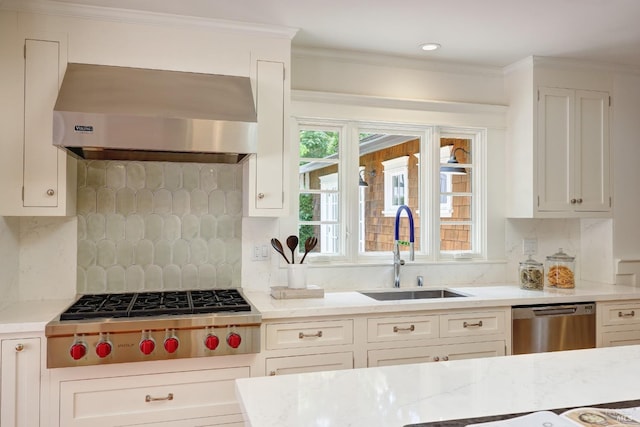 kitchen with appliances with stainless steel finishes, tasteful backsplash, a sink, white cabinets, and extractor fan