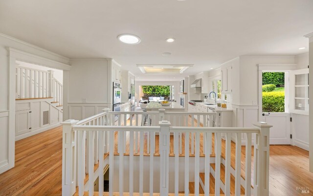 corridor with light wood-style floors, a sink, crown molding, and a decorative wall