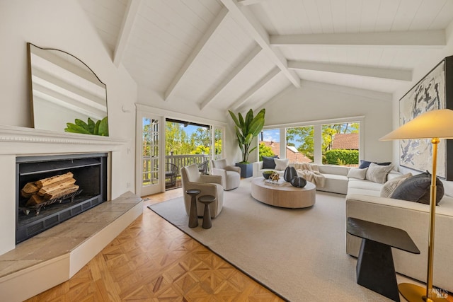 living room featuring lofted ceiling with beams, a fireplace with raised hearth, and a wealth of natural light