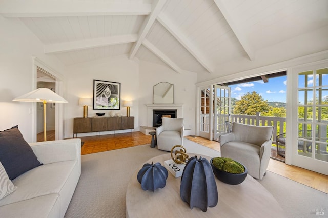 living room featuring vaulted ceiling with beams, a fireplace with raised hearth, and wood finished floors