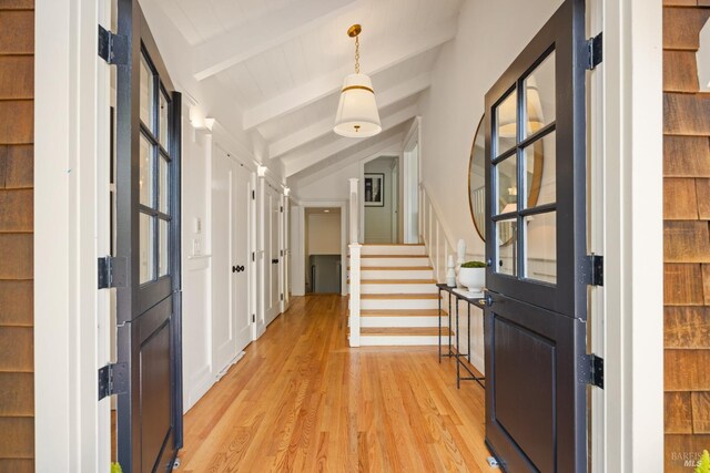 foyer entrance featuring lofted ceiling with beams, light wood-style flooring, and stairway