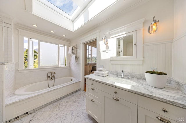 bathroom featuring wainscoting, vanity, marble finish floor, a skylight, and a garden tub