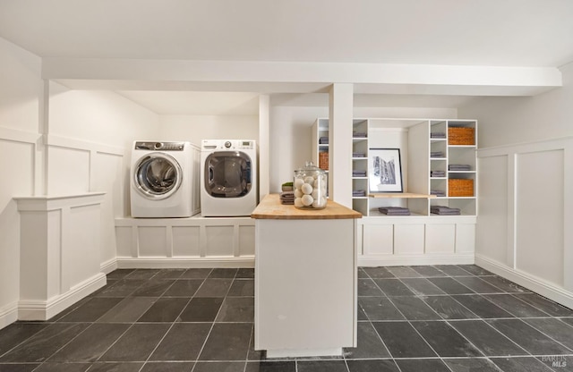 clothes washing area featuring independent washer and dryer, dark tile patterned flooring, wainscoting, and a decorative wall
