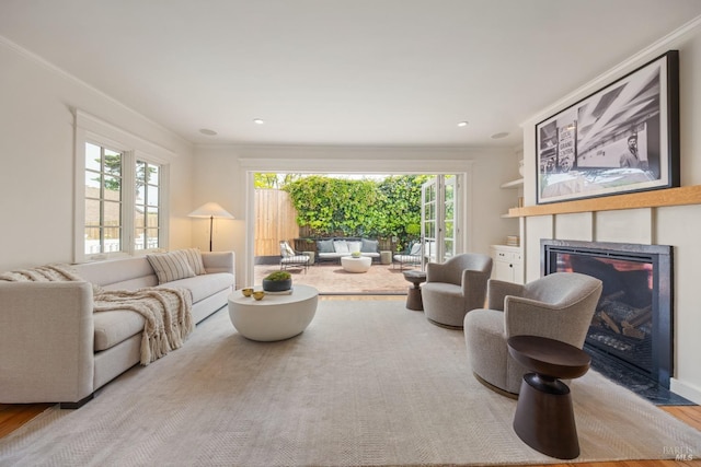 living room featuring a glass covered fireplace, crown molding, wood finished floors, and a healthy amount of sunlight