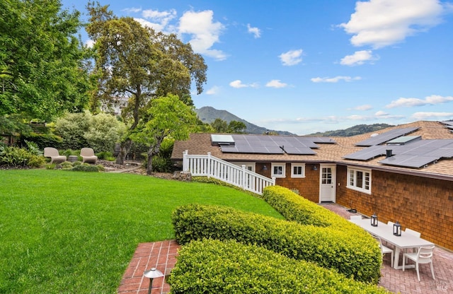 exterior space with a lawn, a mountain view, solar panels, and roof with shingles