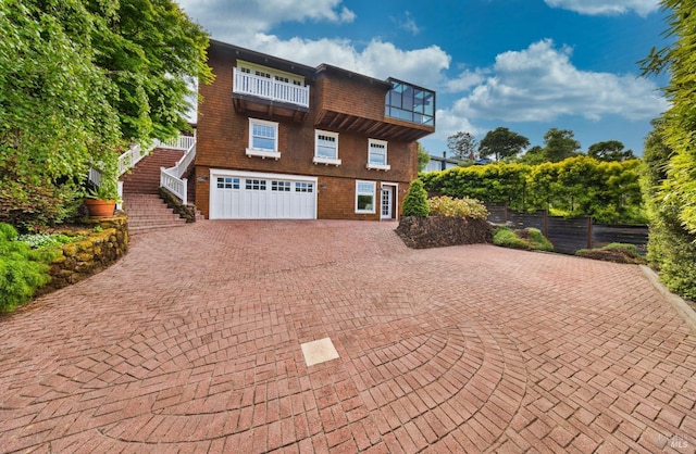 view of front of property featuring fence, a garage, stairway, decorative driveway, and a balcony